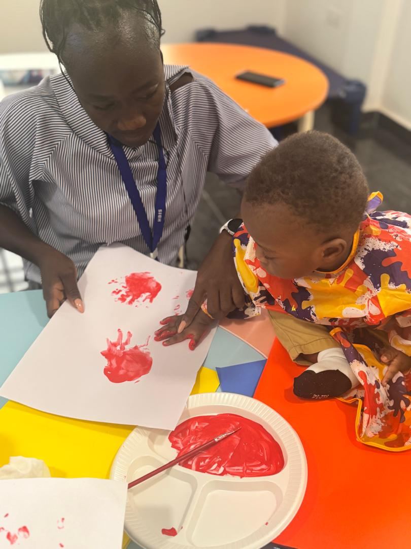 Young child creating handprint artwork with teacher support